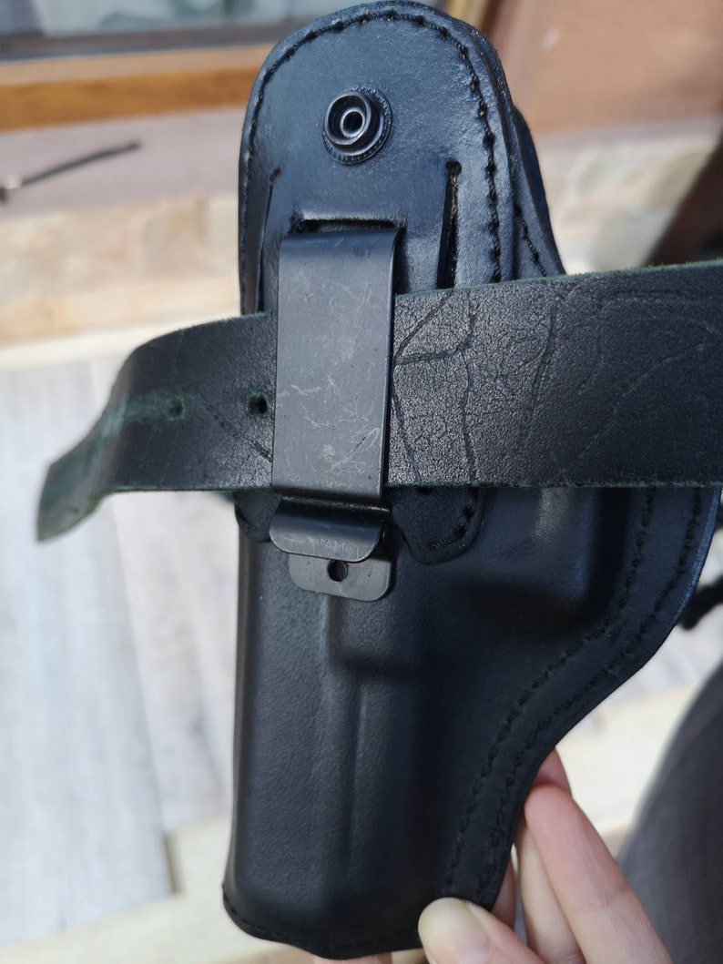 Puede incluir: Funda de cuero negra con un bucle para el cintur&oacute;n y un clip de metal. La funda est&aacute; dise&ntilde;ada para sostener una pistola.