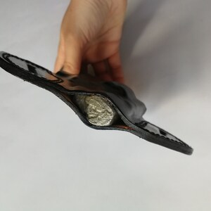 May include: A black leather holster with a silver object inside.