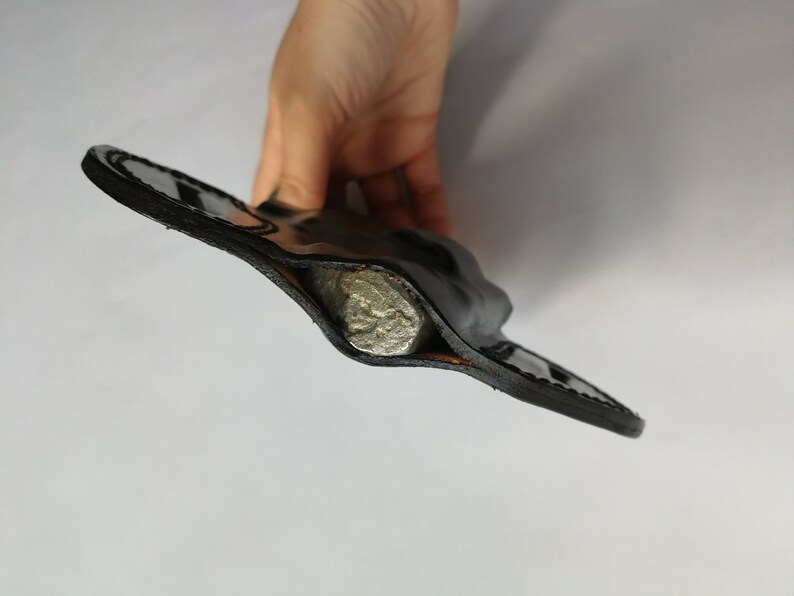 May include: A black leather holster with a silver object inside.
