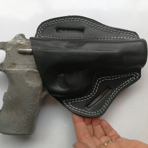 Puede incluir: Una funda de cuero negra con costuras blancas para una pistola. La funda est&aacute; dise&ntilde;ada para llevarla en el cintur&oacute;n.