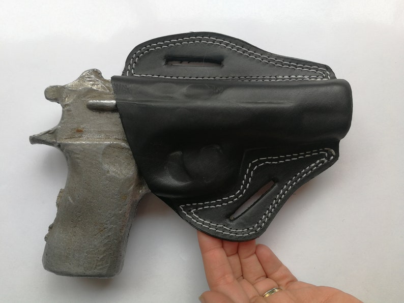 Puede incluir: Una funda de cuero negra con costuras blancas para una pistola. La funda est&aacute; dise&ntilde;ada para llevarla en el cintur&oacute;n.