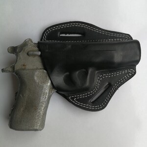 Puede incluir: Una funda de cuero negra con costuras blancas para una pistola. La funda est&aacute; dise&ntilde;ada para llevarla en el cintur&oacute;n.