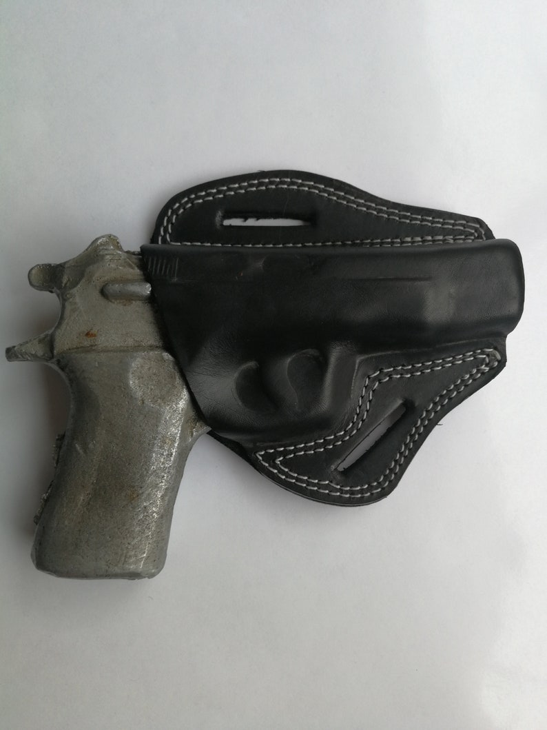 Puede incluir: Una funda de cuero negra con costuras blancas para una pistola. La funda est&aacute; dise&ntilde;ada para llevarla en el cintur&oacute;n.