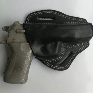 Puede incluir: Una funda de cuero negra con costuras blancas para una pistola. La funda est&aacute; dise&ntilde;ada para llevarla en el cintur&oacute;n.