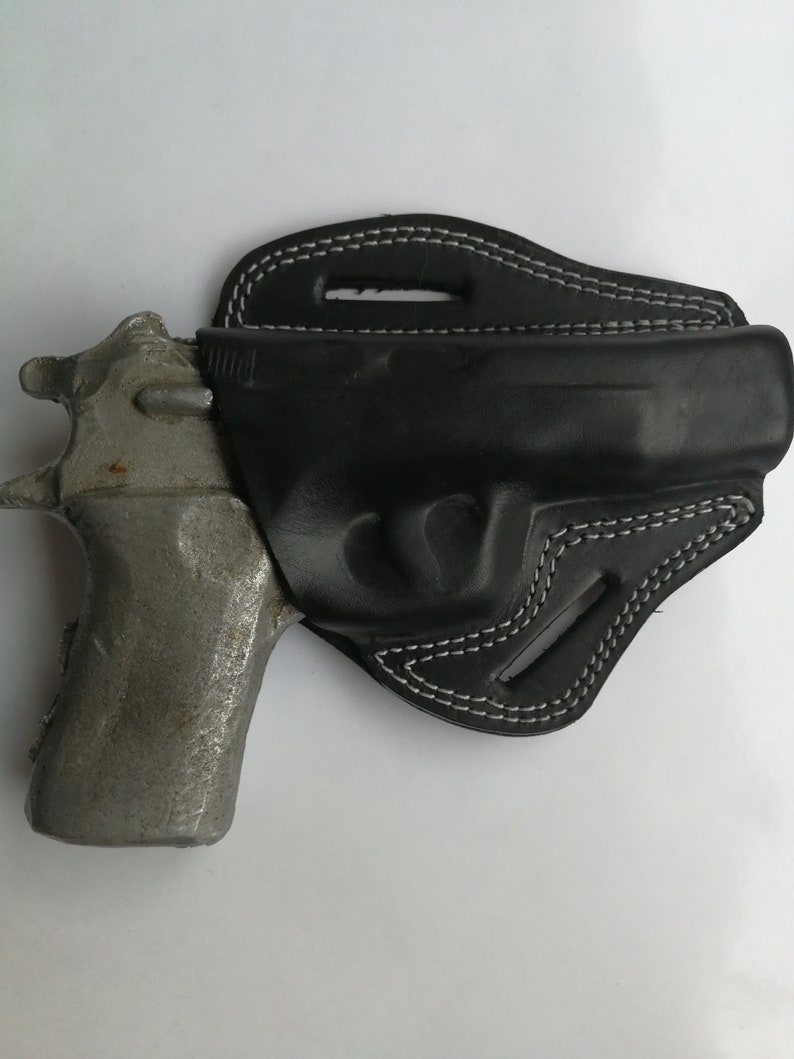 Puede incluir: Una funda de cuero negra con costuras blancas para una pistola. La funda est&aacute; dise&ntilde;ada para llevarla en el cintur&oacute;n.