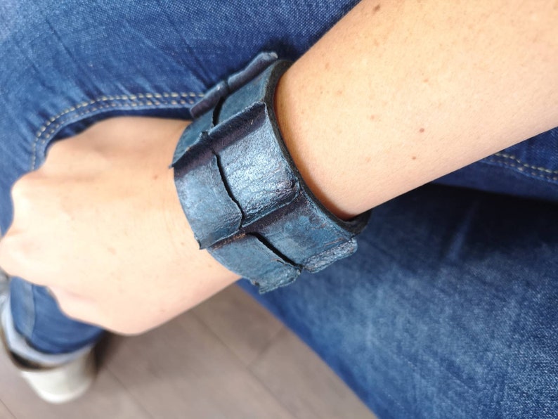 Puede incluir: Un brazalete de cuero azul con un dise&ntilde;o geom&eacute;trico. El brazalete est&aacute; hecho de varias piezas de cuero que est&aacute;n cosidas juntas.