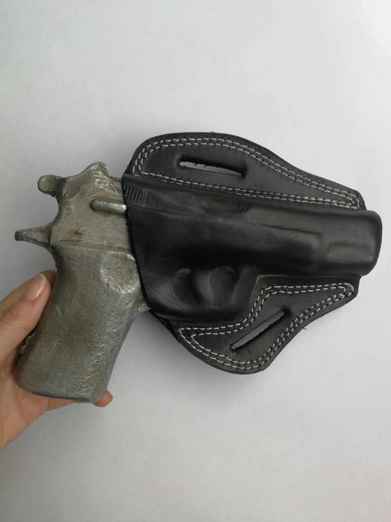 Puede incluir: Una funda de cuero negra con costuras blancas para una pistola. La funda tiene un bucle para el cintur&oacute;n y una traba para el pulgar.