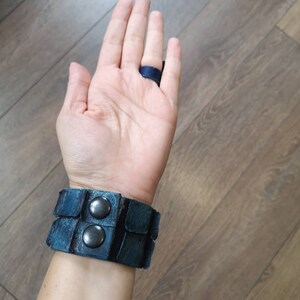 Puede incluir: Un brazalete de cuero azul con dos broches de metal plateado. El brazalete se lleva en la mu&ntilde;eca.