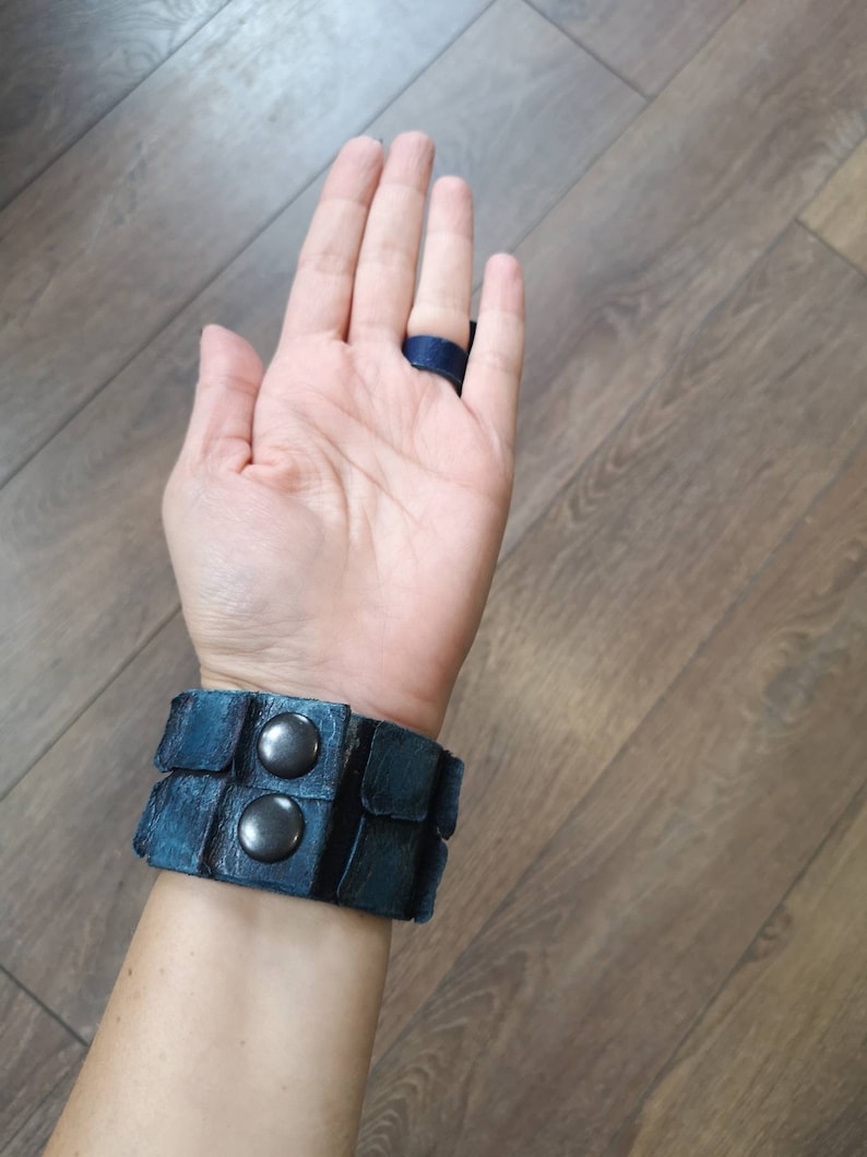 Puede incluir: Un brazalete de cuero azul con dos broches de metal plateado. El brazalete se lleva en la mu&ntilde;eca.