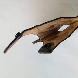 May include: A black leather holster with a brown lining. The holster is open and the lining is visible. The holster has two metal snaps.