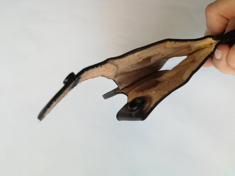 May include: A black leather holster with a brown lining. The holster is open and the lining is visible. The holster has two metal snaps.