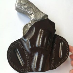 May include: A brown leather holster for a revolver. The holster has a belt loop and a flap that covers the trigger guard.