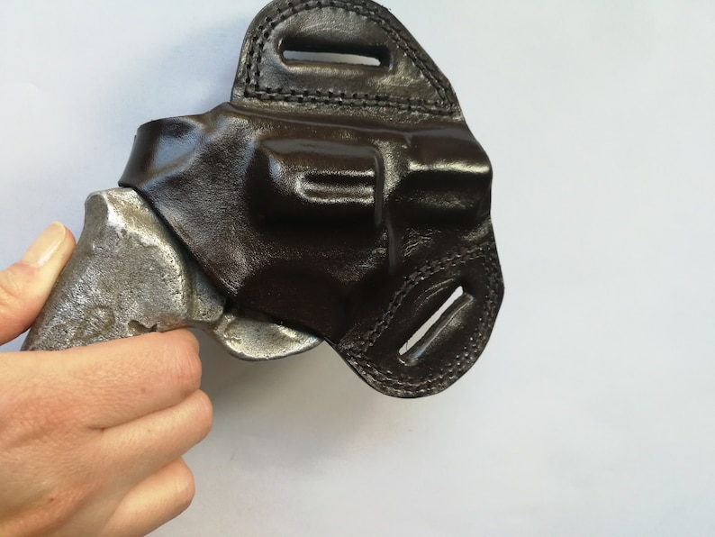 May include: A black leather holster for a handgun. The holster has a belt loop and a snap closure.