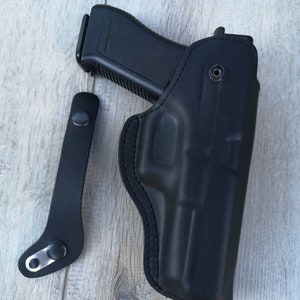 Puede incluir: Una funda de cuero negra para una pistola con una correa negra.