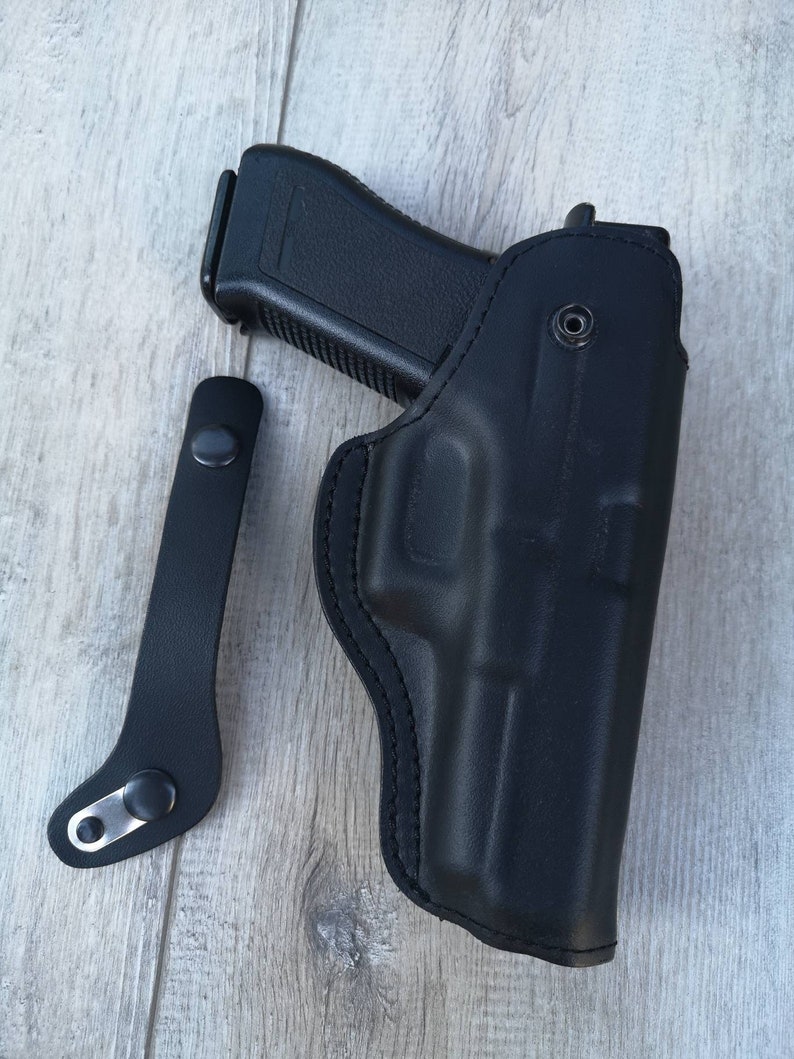 Puede incluir: Una funda de cuero negra para una pistola con una correa negra.