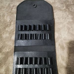 Könnte beinhalten: Schwarze Ledertasche mit mehreren Fächern zum Aufbewahren von kleinen Gegenständen wie Stiften oder Bleistiften.