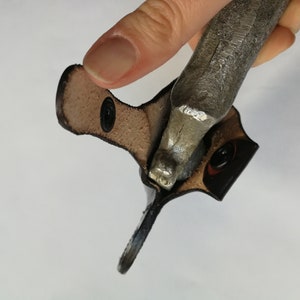 May include: A brown leather case with a metal object inside. The case has two black snaps.