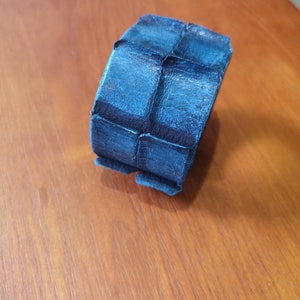 Puede incluir: Un brazalete de cuero azul oscuro con un dise&ntilde;o texturizado y geom&eacute;trico.