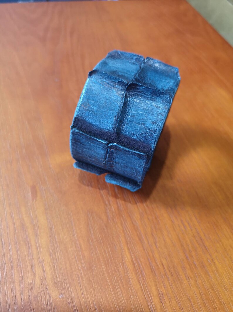 Puede incluir: Un brazalete de cuero azul oscuro con un dise&ntilde;o texturizado y geom&eacute;trico.