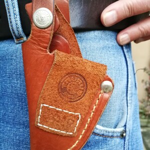 Pode incluir: Um coldre de couro marrom com detalhes de costura branca e um bot&atilde;o prateado. O coldre tem um logotipo circular com a palavra "BRASIL" impressa nele.