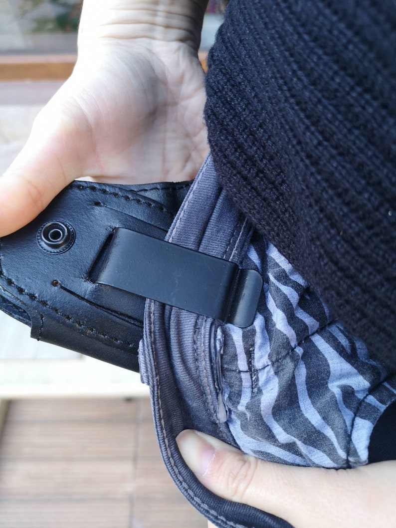 Puede incluir: Una funda de cuero negra con un clip met&aacute;lico sujeto a un pantal&oacute;n de rayas blancas y negras.