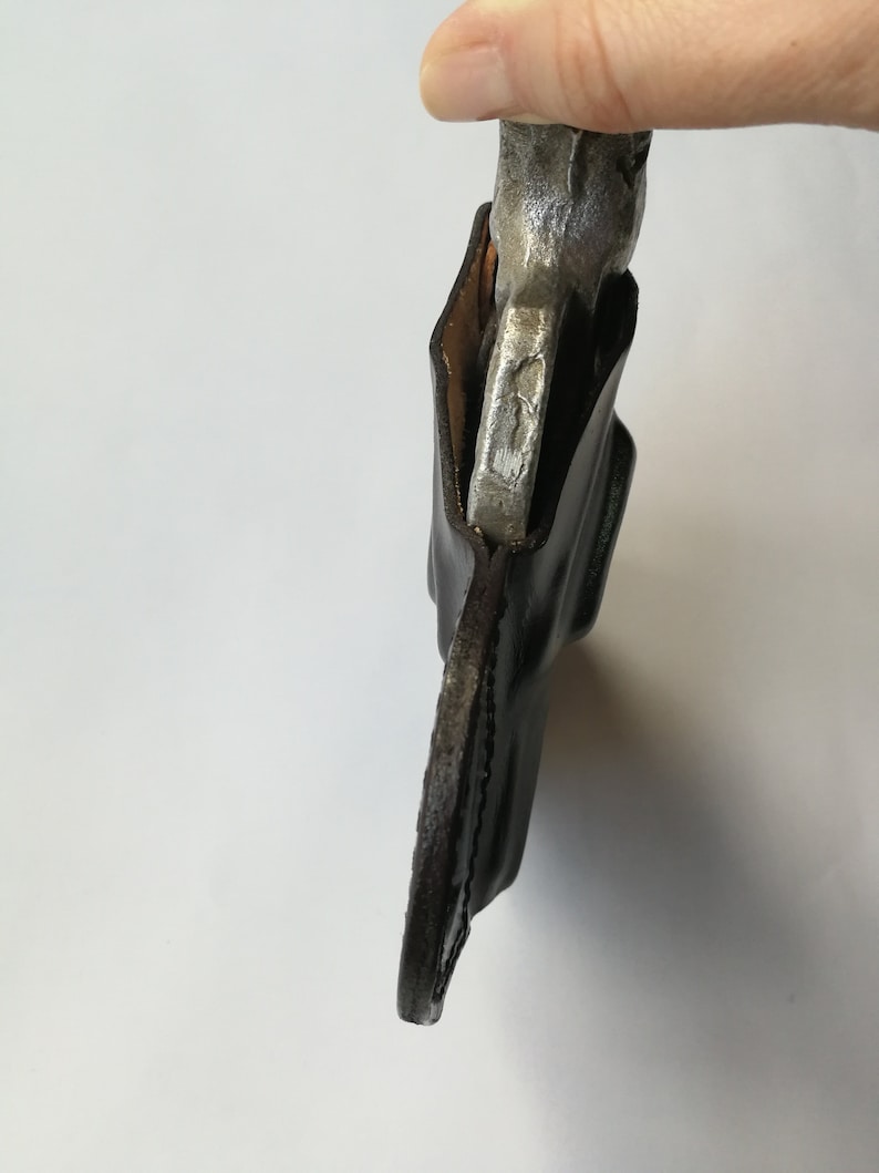 May include: A brown leather holster with a silver metal object inside. The holster is designed to hold a small tool or weapon.