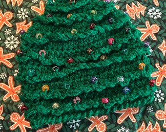 May include: A green crocheted Christmas tree hat with colorful beads. The hat is on a green background with a gingerbread man pattern.