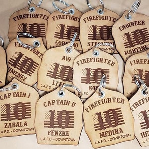 May include: A collection of brown leather keychains with the text "Firefighter" and "Engineer" and the number "10" printed on them. Each keychain has a different name and the text "L.A.F.D. - Downtown" printed on them.