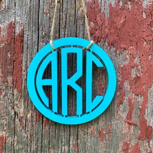 May include: A teal blue wooden circle with the letters "ARC" cut out in a black font. The circle is hanging from a piece of twine.