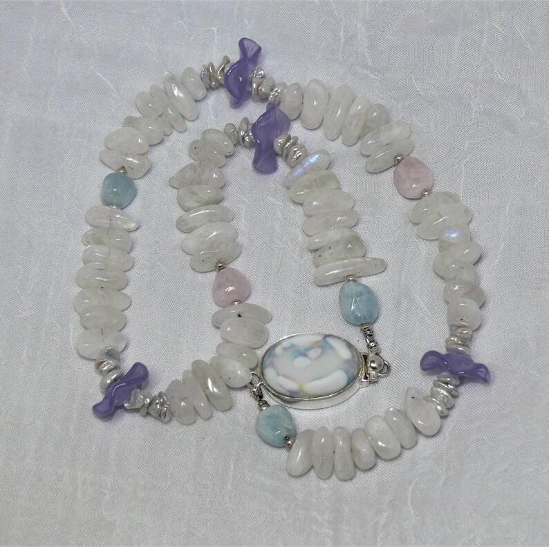 May include: A white moonstone necklace with a silver clasp and a variety of gemstone accents, including lavender, pink, and blue.