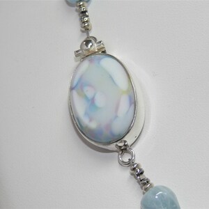 May include: A silver necklace with a large oval pendant featuring a blue and white marbled glass design. The pendant is attached to a silver chain with smaller beads.