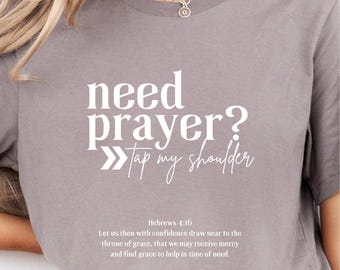 Puede incluir: Una camiseta gris con el texto "need prayer? Tap my shoulder" en blanco. La camiseta también incluye un versículo bíblico de Hebreos 4:16.
