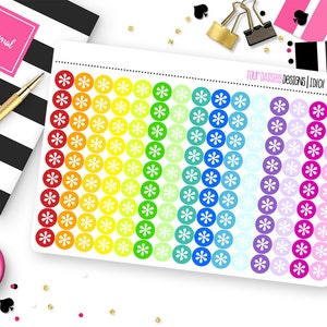 May include: A sheet of colorful flower stickers in a rainbow gradient. The stickers are arranged in rows and columns, with each flower inside a circle. The text "FOUR DAISIES DESIGNS | IDIOI" is printed on the top right corner. A journal and pen are in the background.