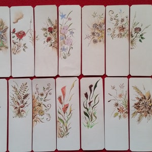 Puede incluir: Conjunto de 16 marcap&aacute;ginas en blanco con dise&ntilde;os florales pintados a mano. Cada marcap&aacute;ginas presenta un motivo floral diferente en tonos rojos, azules, amarillos y verdes.
