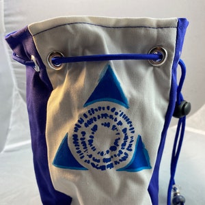 May include: A blue and white drawstring bag with a geometric design. The bag features a blue triangle and circular pattern on a white background, with blue sides. It has a blue drawstring and decorative beads.