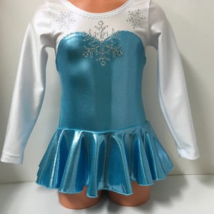 May include: A light blue and white long-sleeved leotard with a flared skirt, embellished with silver rhinestones in a snowflake design. The bodice is a metallic blue, and the sleeves are white. This costume is designed for dance or ice skating.