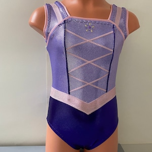 May include: A purple and pink leotard with a criss-cross design on the bodice and a star-shaped embellishment. The leotard has a scoop neck and a sleeveless design.