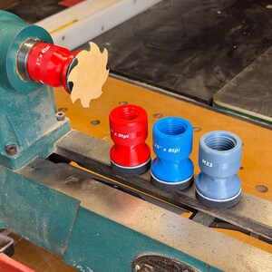 May include: A set of four cylindrical lathe chuck adapters in red, blue, and gray, featuring knurled grips and threaded interiors. One red adapter is attached to a green lathe, while three others sit on the lathe bed, labeled 1 inch x 8tpi, 1.25 inch x 8tpi, and M33.