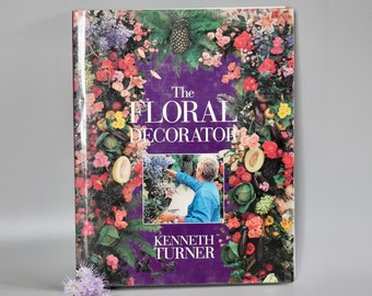 May include: A purple book titled "The Floral Decorator" by Kenneth Turner. The cover features a colorful floral arrangement with a person in the center.