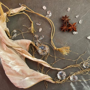 May include: A white silk scarf with gold trim and tassels, tied with a brown cord. The scarf is decorated with clear crystal beads and star anise.