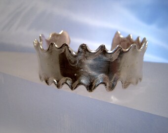 May include: A silver bracelet with a wavy, scalloped edge. The bracelet is made of metal and has a shiny finish.