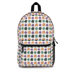 Puede incluir: Una mochila blanca con un patrón repetido de calabazas de colores. Las calabazas son de color naranja, verde y morado. La mochila tiene una cremallera negra y un bolsillo de malla en el lateral.