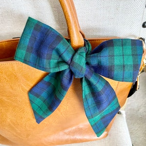 May include: A brown leather handbag with a green and blue plaid bow tied around the handles.