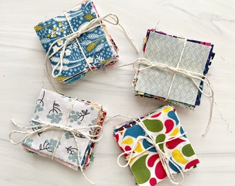 May include: Four bundles of fabric squares, each tied with twine. The fabric squares are in various patterns and colors, including blue, green, red, yellow, and white.