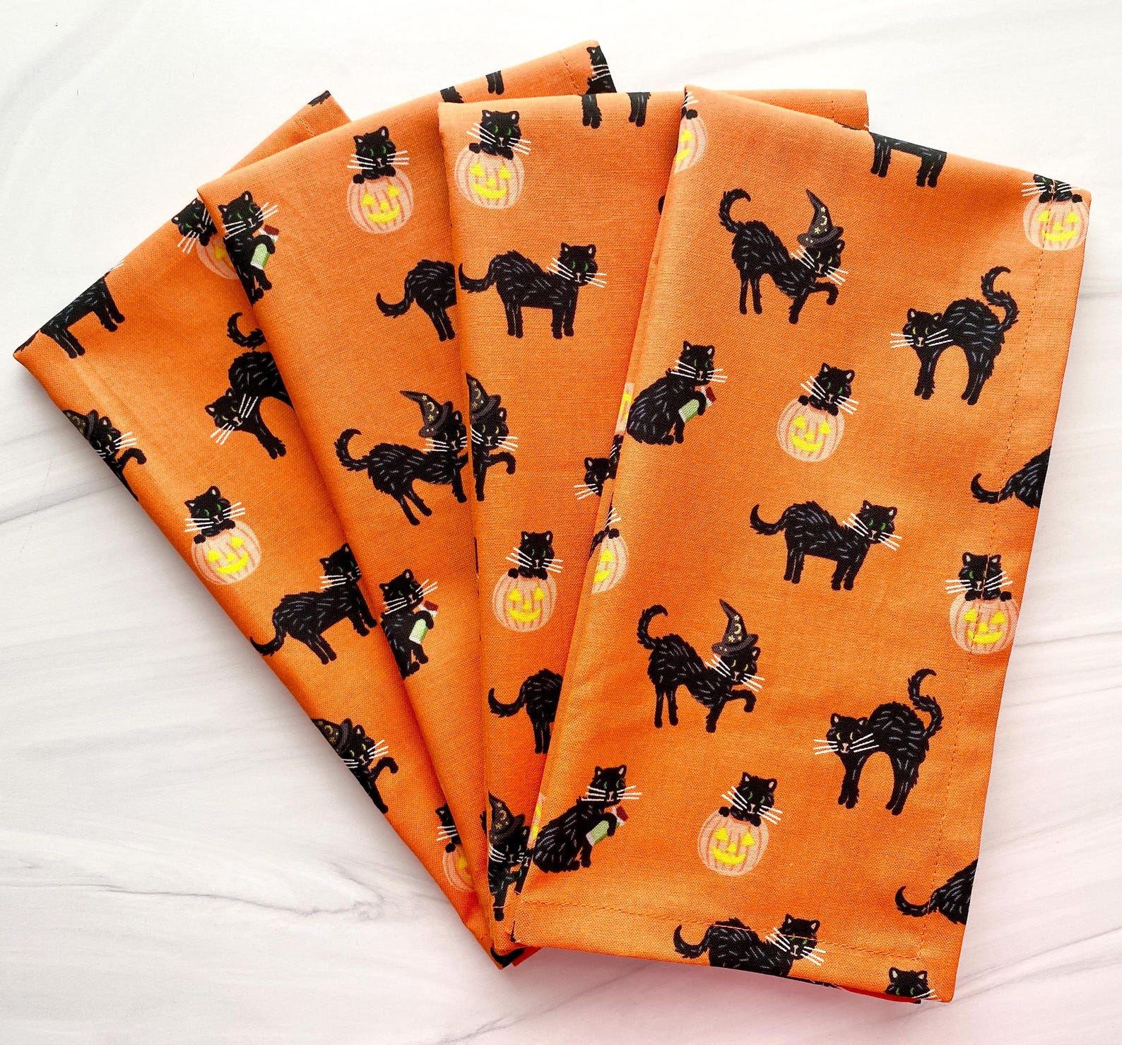 A Plain Fold that Lets the Print Work Orange cloth napkins with a repeating black-cat Halloween pattern.