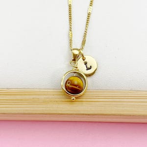May include: Gold necklace with a spinning tiger's eye stone pendant and a gold charm with the letter 'L' on it.
