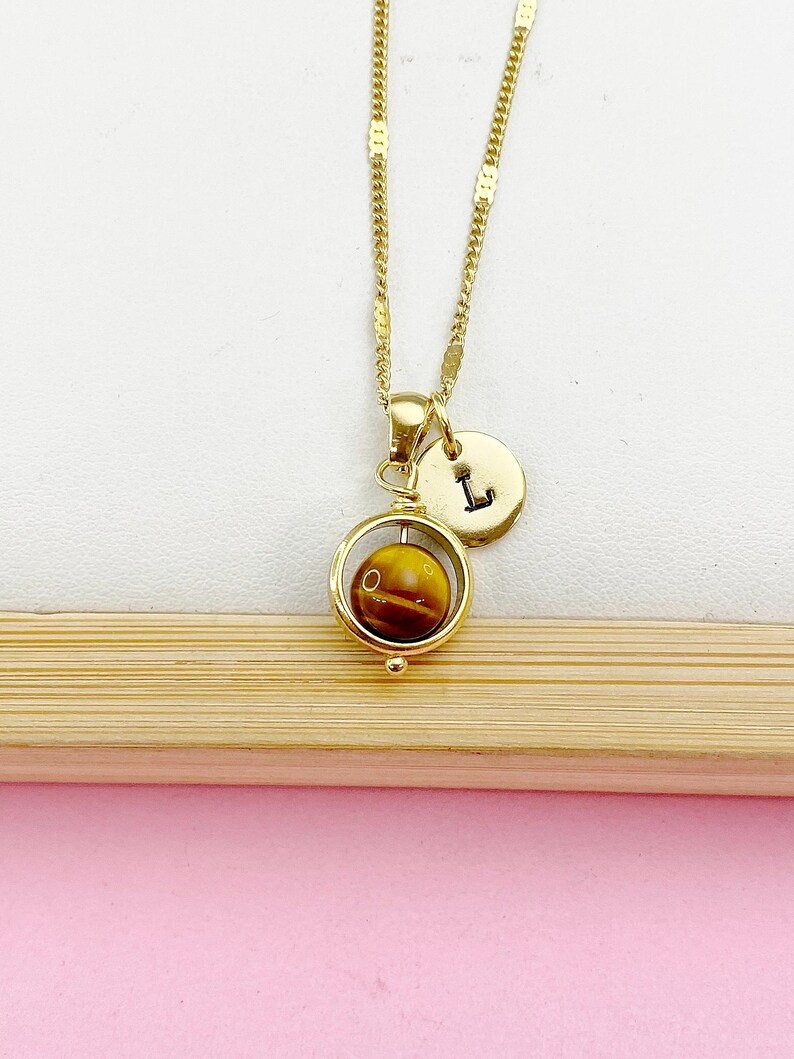 May include: Gold necklace with a spinning tiger's eye stone pendant and a gold charm with the letter 'L' on it.