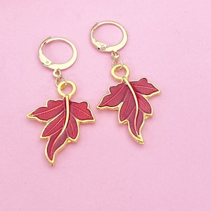 May include: A pair of gold earrings with red leaf designs. The leaves are detailed with gold veins and have a glossy finish.