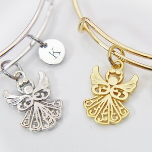 K&ouml;nnte beinhalten: Zwei dehnbare Armreifen mit Engelsanh&auml;ngern und personalisierten Buchstaben-Scheiben. Das Armband links ist silberfarben mit einem silbernen Engelsanh&auml;nger und einer Scheibe mit dem Buchstaben "K". Das Armband rechts ist golden mit einem goldenen Engelsanh&auml;nger und einer Scheibe mit dem Buchstaben "E".