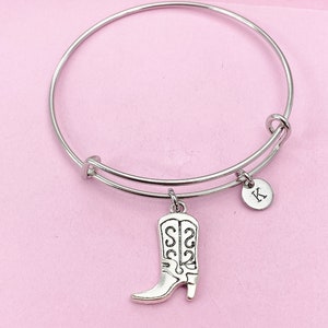 May include: A silver expandable bangle bracelet with a charm of a silver cowboy boot and a silver charm with the letter K.